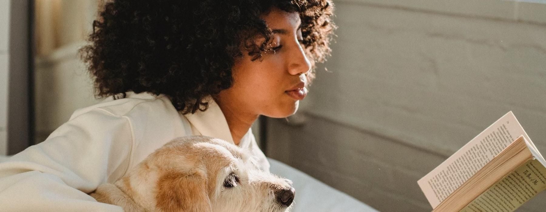 a person reading a book while laying next to a dog